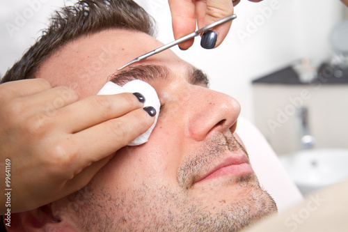 Fototapeta Naklejka Na Ścianę i Meble -  Beautician plucking a beautiful man eyebrows with tweezers in a