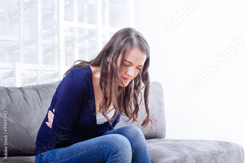  Young Woman Sitting On Sofa Suffering From stomach ache