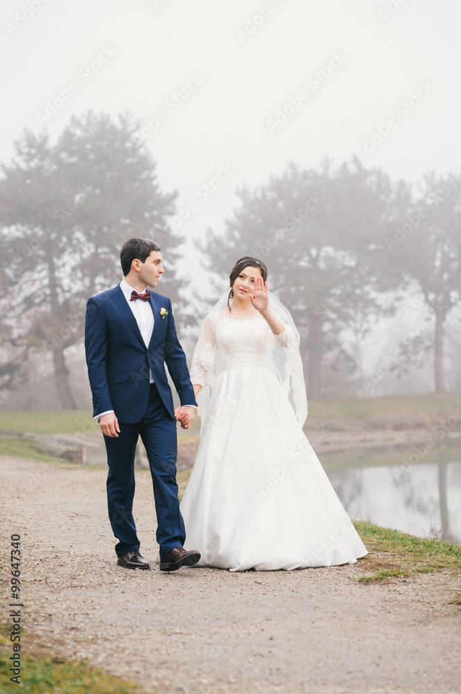 bride and groom are walking by the lake