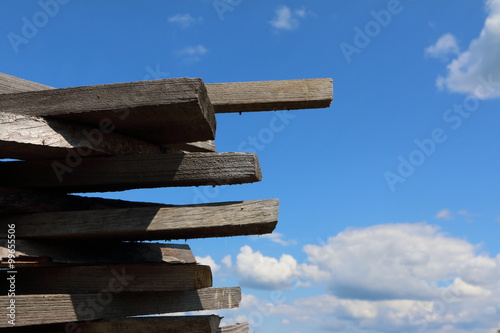 Ends of the rough pine boards in the outdoor stack against a blue sky photo