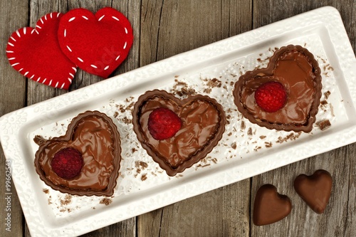 Heart shaped chocolate cups filled with pudding and raspberries on a plate with rustic wood background photo