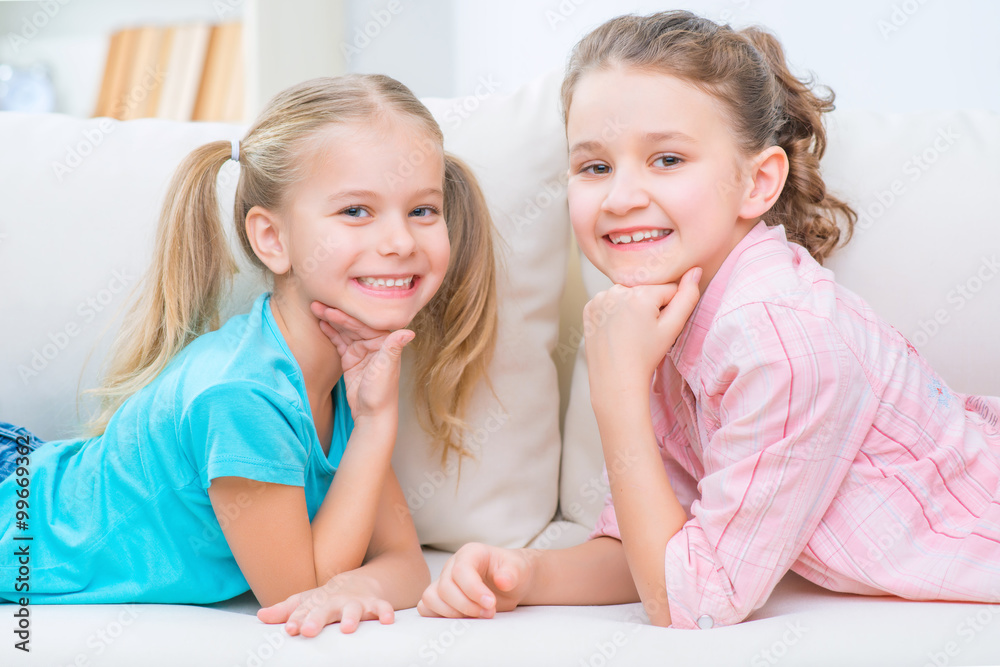 Cheerful little sisters sitting on the sofa Cheerful little sisters sitting on the sofa
