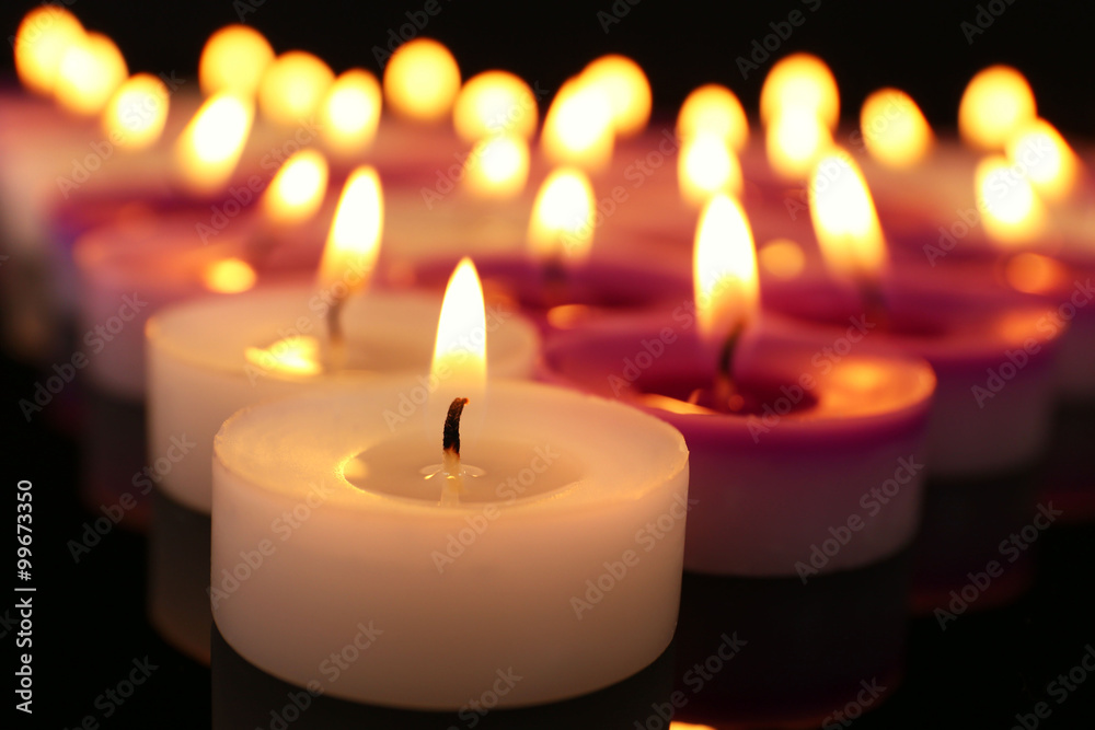 Many burning small candles on dark background, close-up