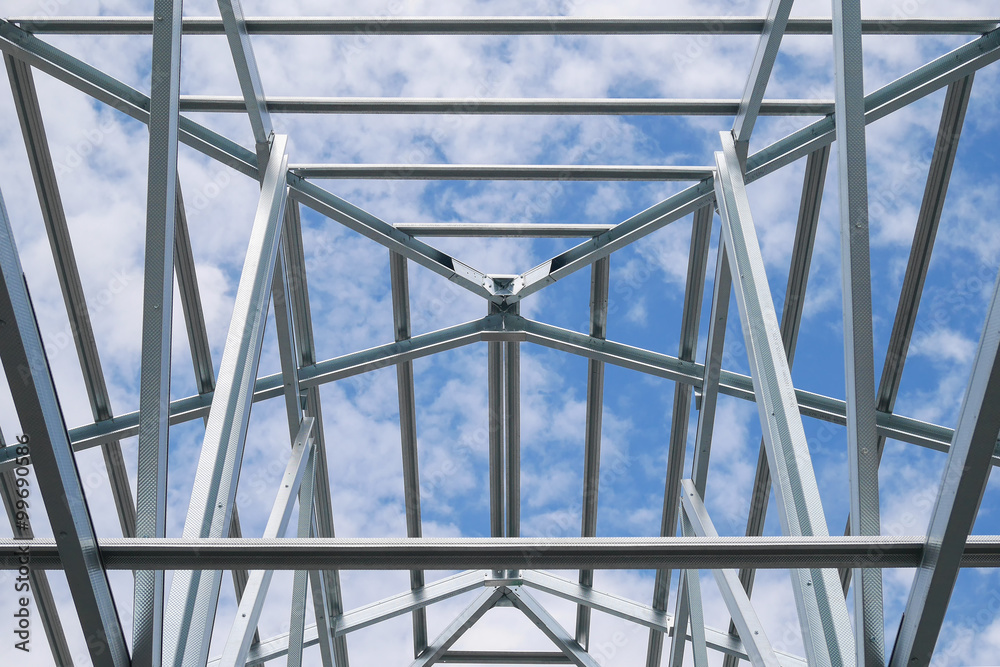 Fototapeta premium Structure of steel roof frame with blue sky and clouds at construction site