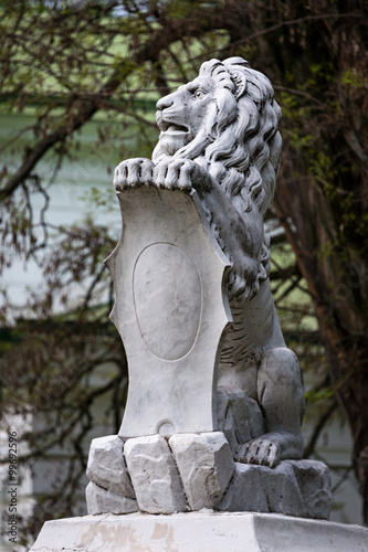 Statue of lion holding a shield in its paws. Regal lion leaning on empty heraldic shield.