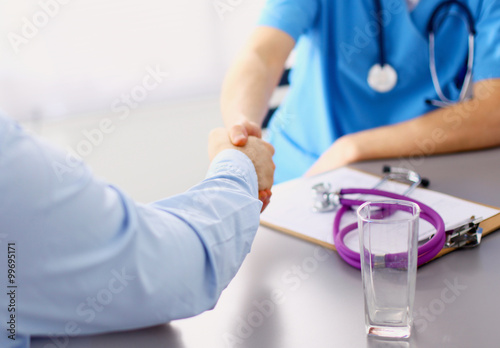 Attractive female doctor shaking a patient's hands in her office