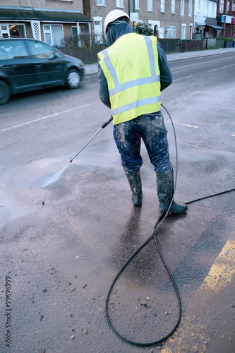 Construction worker cleaning street with water hose