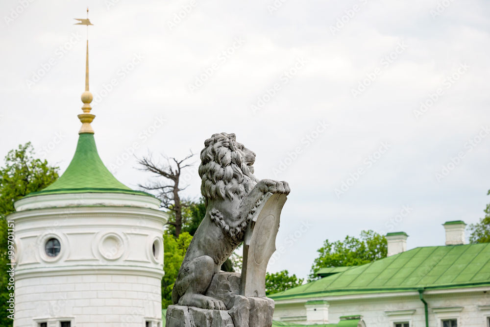 Obraz premium Statue of lion holding a shield in its paws. Regal lion leaning on empty heraldic shield near the castle entrance. The palace and park complex Manor Tarnowski, s.Kachanovka, Ukraine.