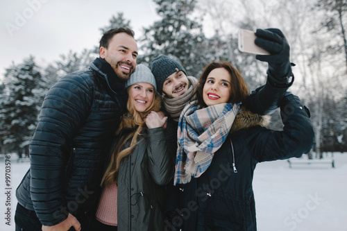 Cute young hipster couples posing in winter park on a bright day hugging each other and smiling
