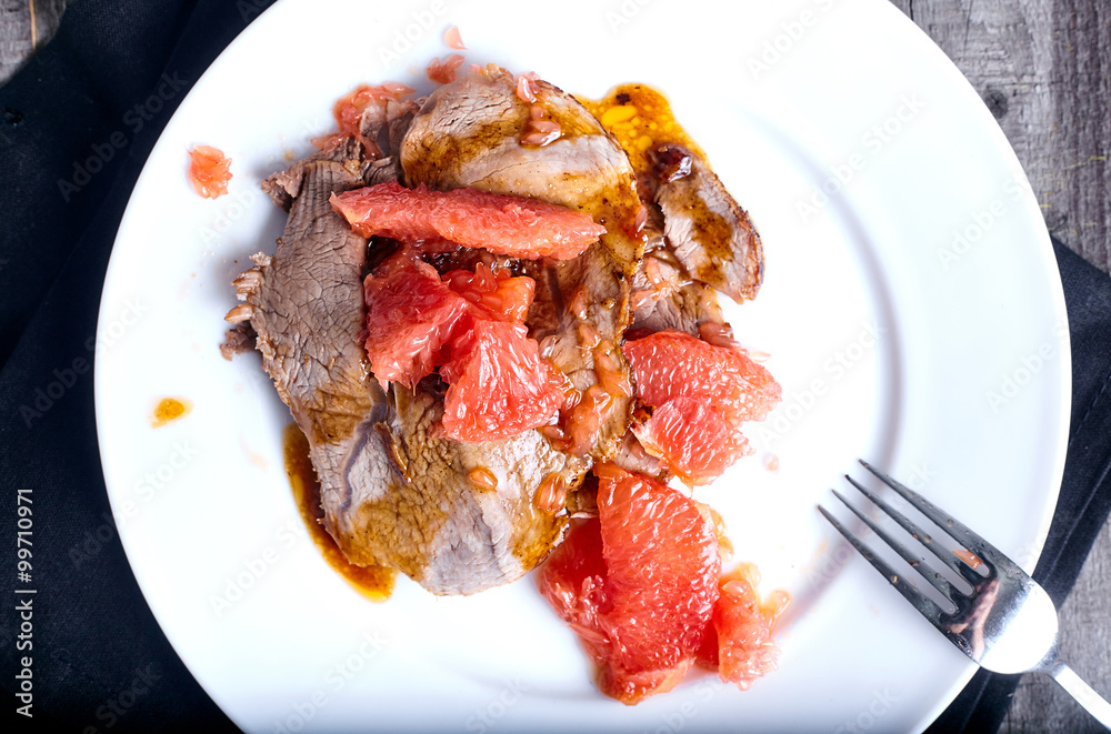 Beef with grapefruit sauce on wood background