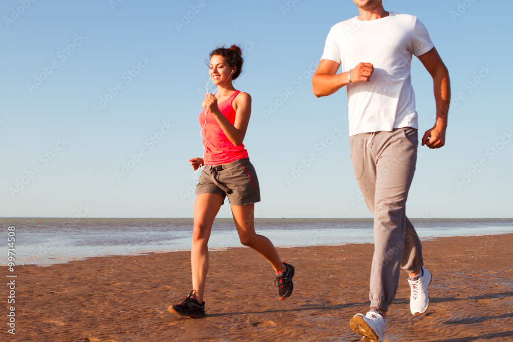 Fototapeta premium Young couple running together beside the water at the beach. Man