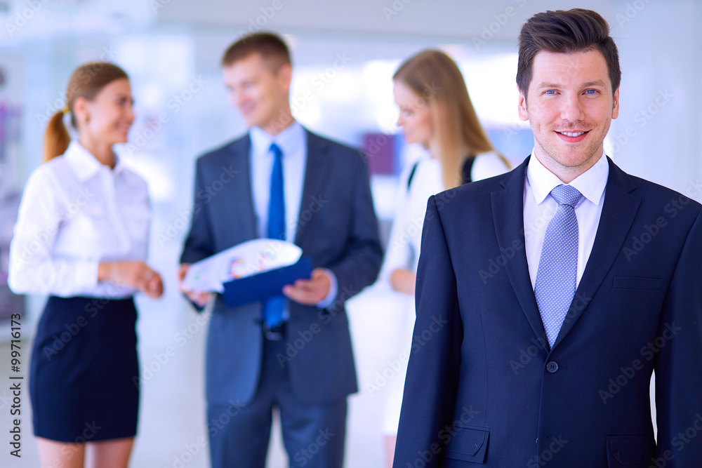 Portrait of young businessman in office with colleagues in the background Portrait of young businessman in office with colleagues in the background