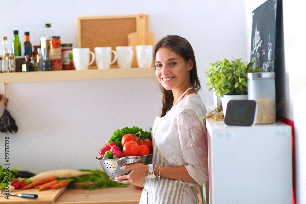 Smiling young woman holding vegetables standing in kitchen Smiling young woman holding vegetables standing in kitchen