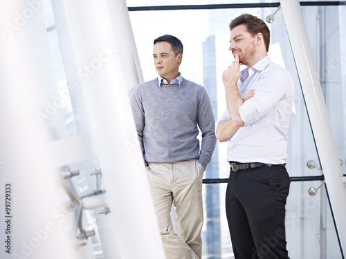two caucasian businessmen looking out of window