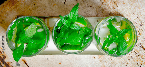 Three cocktail glasses with ice cubes, lime, mint leaves and rum . On the old background.