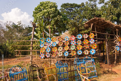 Roadside marketplace with handmade traditional plait collars on window and chairs before against blossoming tree and blue sky background. Uganda, Eastern Africa.
