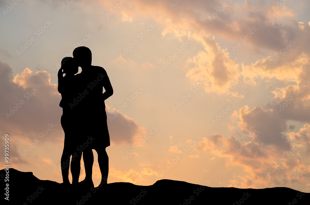 Silhouette of romantic a couple hug kissing against a sunset sky