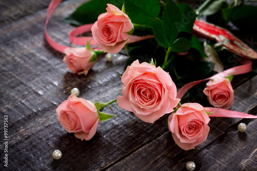 Beautiful pink roses on a dark wooden table with a pink ribbon