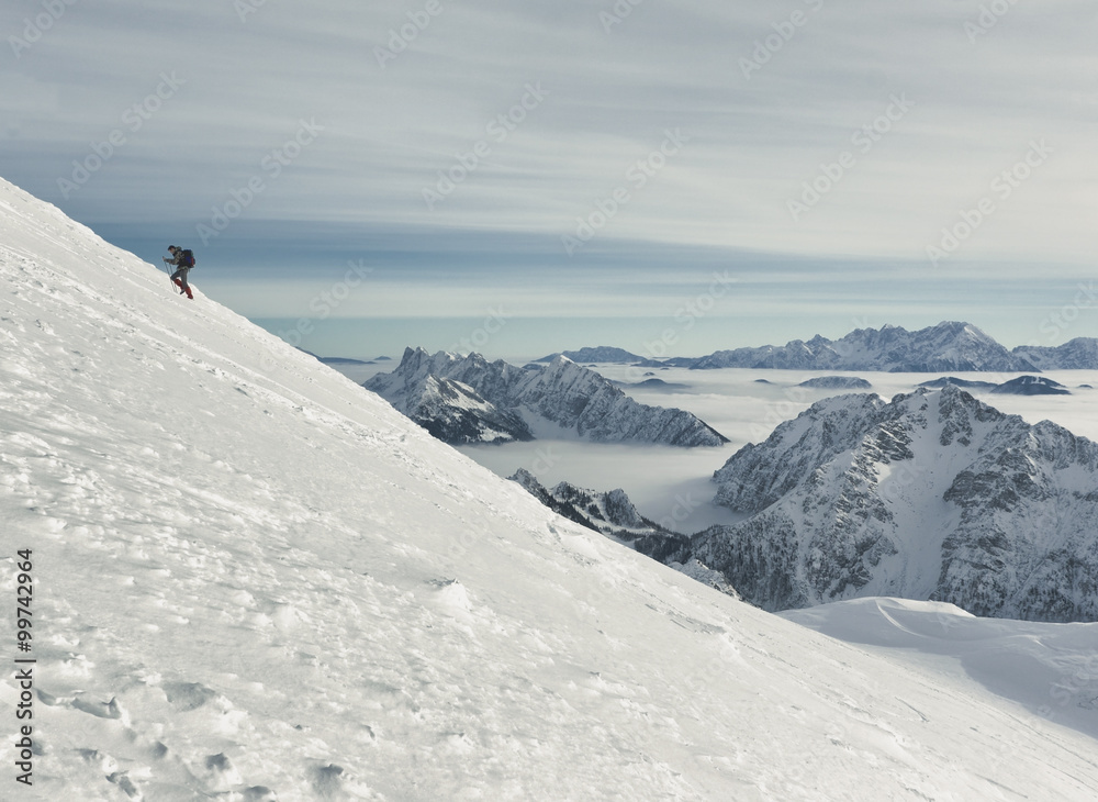 Winter in the mountains; hiker ascending the snowy ridge towards Mt. Stol (2236 m) in Karavanke Alps.