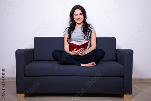 portrait of happy woman sitting on sofa and reading book