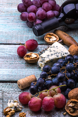 Red wine bottle  grapes  walnuts and cheese on a wooden background