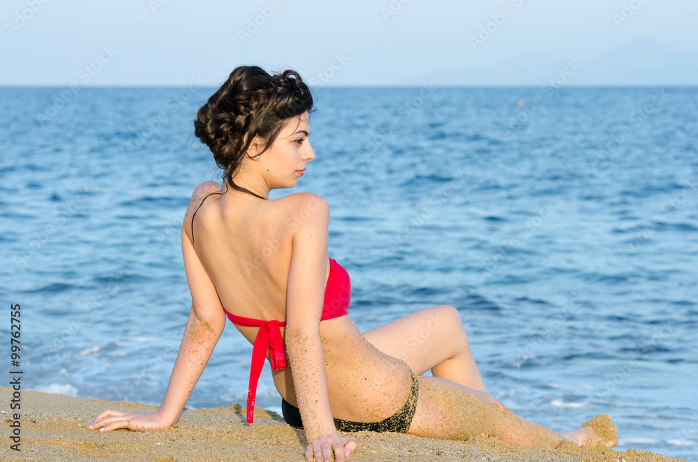 Young slim pretty lady wear red and black bikini sitting on sand and gaze the sea view