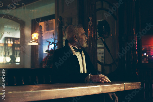 Bearded senior man in tuxedo sitting at table of outdoor cafe.