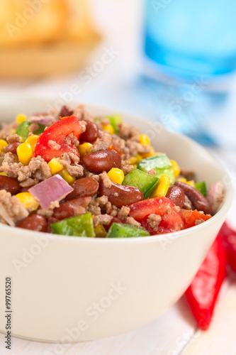 Chili con carne salad made of mincemeat, kidney beans, green bell pepper, tomato, sweet corn and red onions served in bowl with chili on the side (Selective Focus, Focus in the middle of the salad)