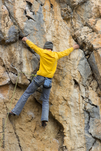 Young male climber hanging by a cliff.