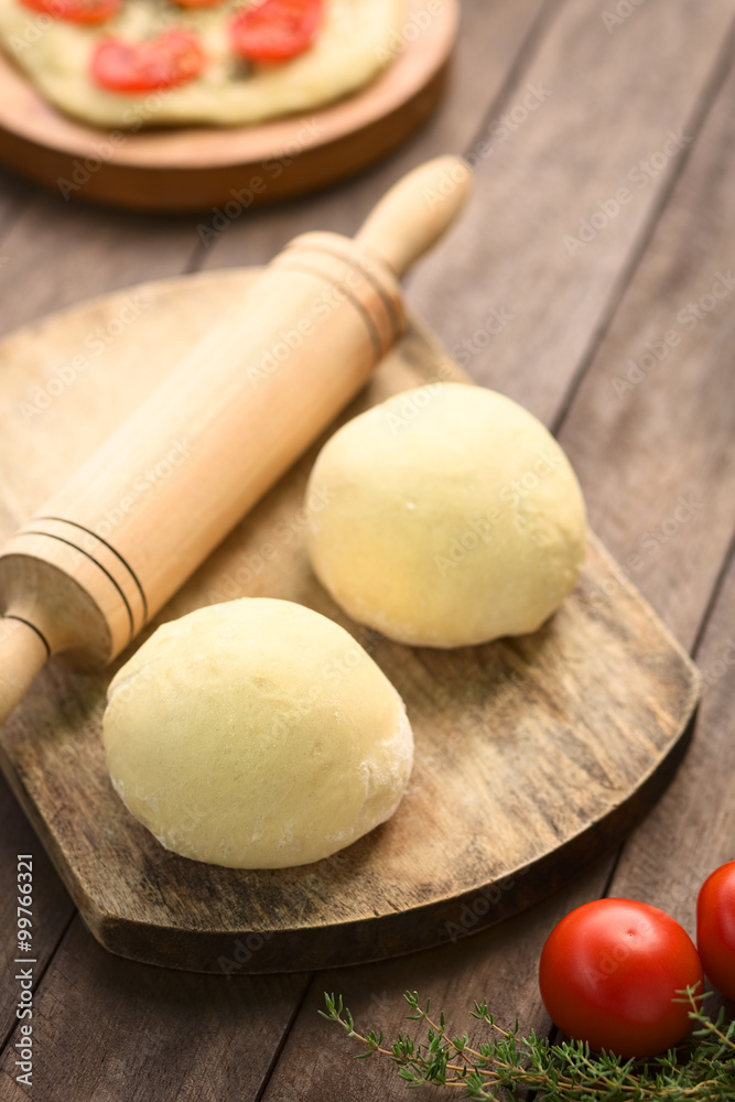 Small balls of yeast dough for pizza or flatbread with rolling pin on wooden board (Selective Focus, Focus on the front of the first dough ball) Small balls of yeast dough for pizza or flatbread with rolling pin on wooden board (Selective Focus, Focus on the front of the first dough ball)
