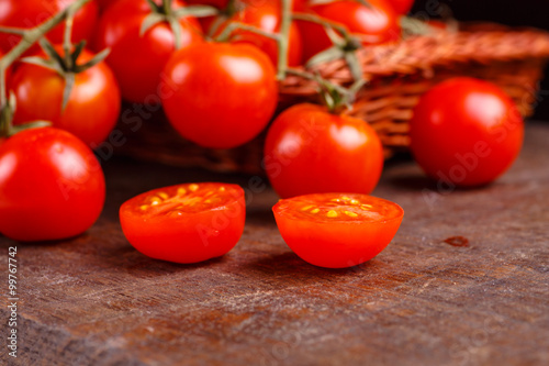 Branch of red tomatoes lying in a basket on a dark table.