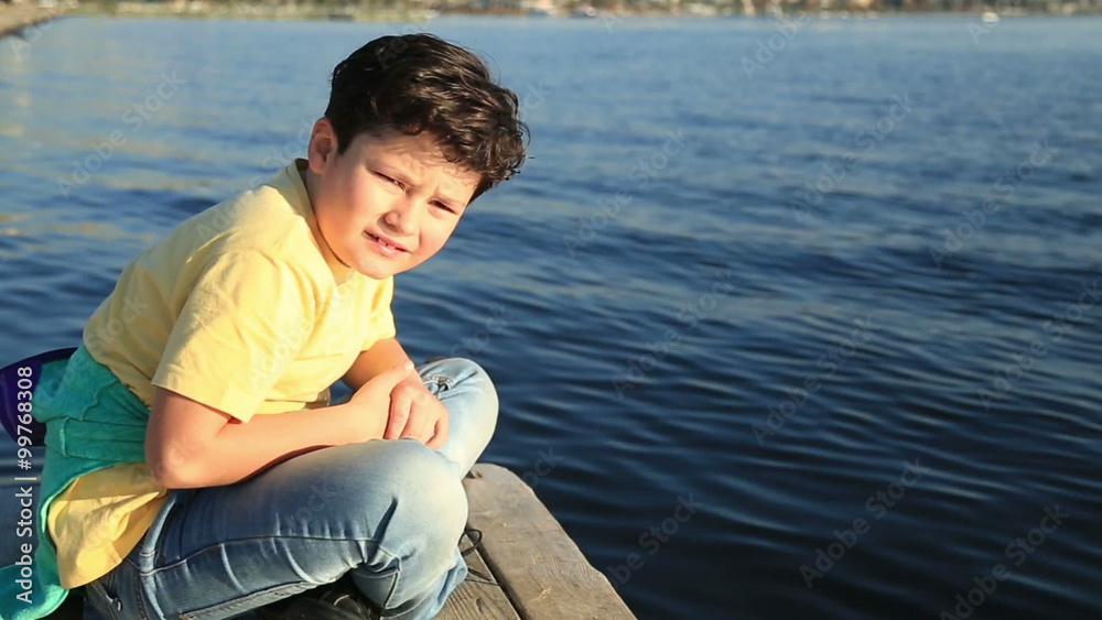 Young boy sits alone in the wooden quay looking at the camera and smiling Young boy sits alone in the wooden quay looking at the camera and smiling