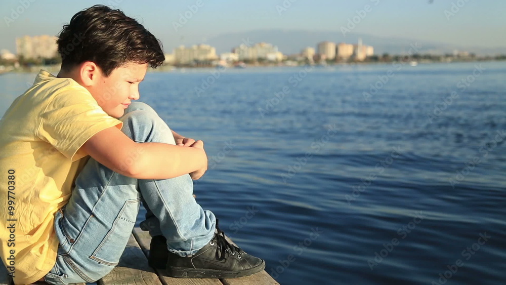 Lonely sad young boy on a wooden quay