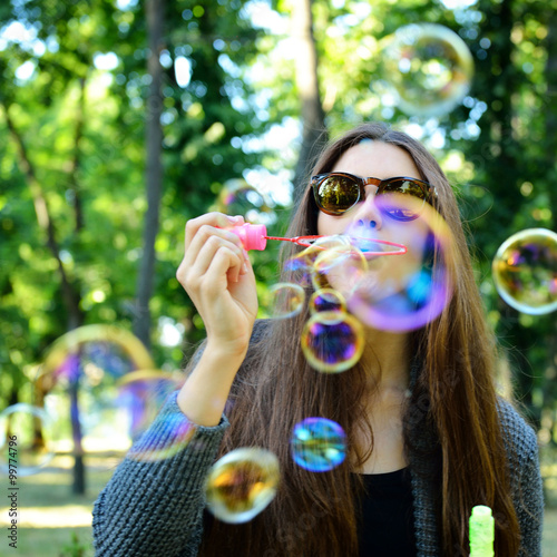 Young woman blowing soap bubbles outdoor in fall park. Image ton