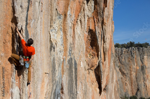 Young man climbs on a rocky wall in a valley with mountains at sunrise.