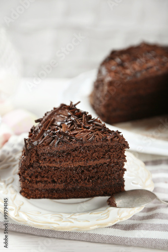 Sliced chocolate cake on wooden table, on light background