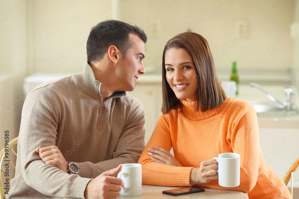 Young man whispering something to his girlfriend's ear while having a cup of coffee Young man whispering something to his girlfriend's ear while having a cup of coffee