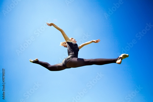 Smiling young gymnast is jumping in split and floating above the
