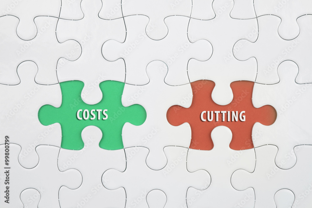 Jigsaw puzzle on color paper background with a word COSTS and CUTTING Jigsaw puzzle on color paper background with a word COSTS and CUTTING