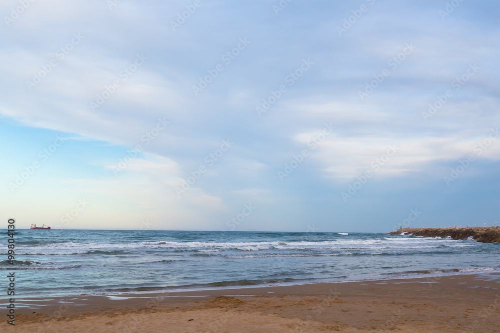 Sandy beach near Valencia, Spain. A beautiful beach with shallow water and a stony breakwater pier.