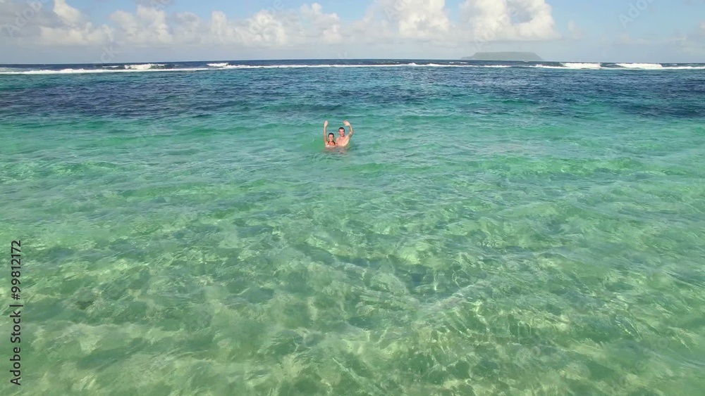 Couple in Caribbean sea waving at drone camera Couple in Caribbean sea waving at drone camera