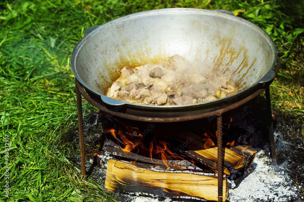 Closeup image of meat stewed in old cauldron at bonfire Closeup image of meat stewed in old cauldron at bonfire