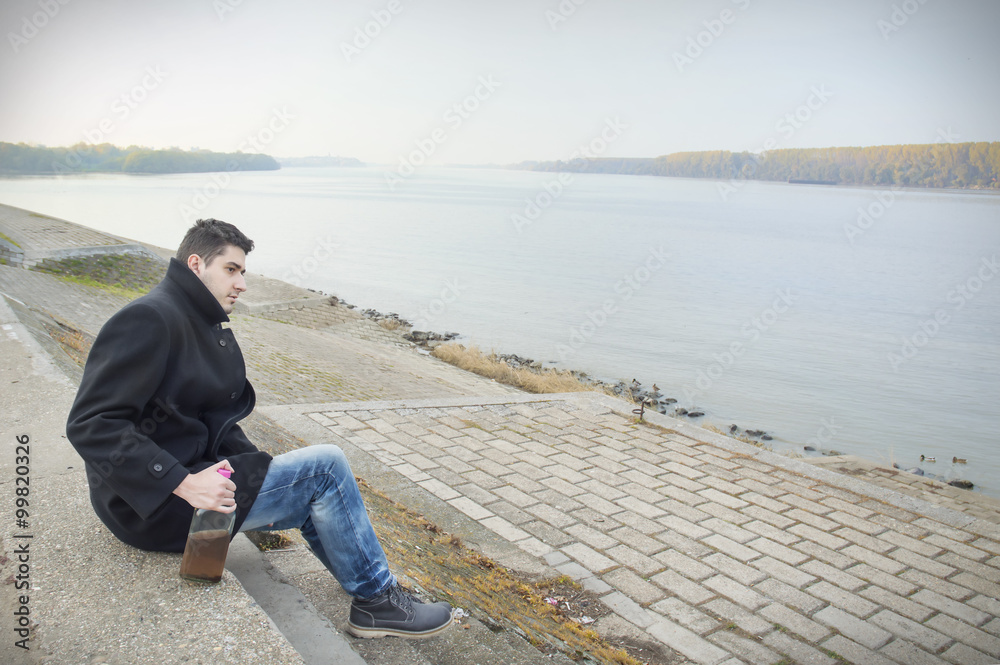 Man thinking and holding bottle of alcohol drink at the riverside Man thinking and holding bottle of alcohol drink at the riverside