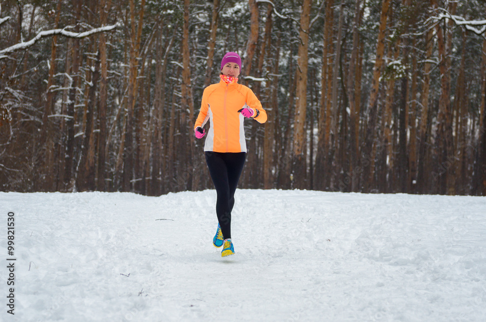 Winter running in forest: happy woman runner jogging in snow, outdoor sport and fitness concept
