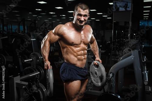 Muscular athletic bodybuilder fitness model posing after exercises in gym