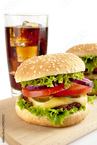 Set of two cheeseburgers and glass of cola on wooden board