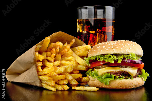 Big cheeseburger with glass of cola and french fries on black desk