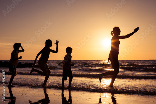 Mother and children playing on the beach at the sunset time.