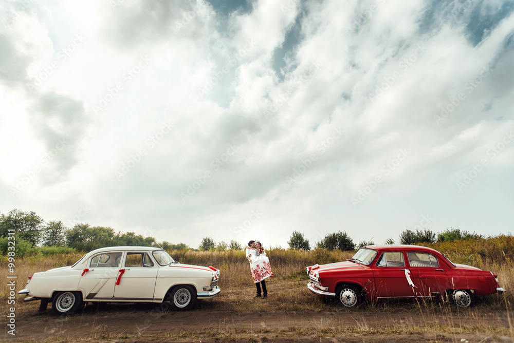 stylish bride and happy groom near  two retro cars on the backgr