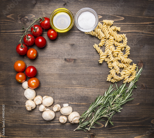 Ingredients for cooking vegetarian raw fusilli pasta with sunflower oil cherry tomatoes, mushrooms, rosemary place for text,frame on wooden rustic background top view
